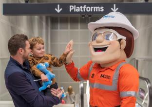 Dad holding son high fiving the Sydney Metro mascot