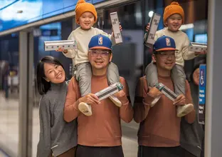 Dad with kid on his shoulder and wife standing next to them all holding cardboard train models