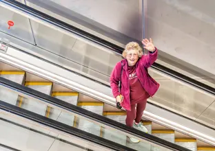 Old lady in a purple jacket going down the escalators waving