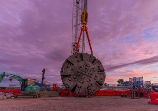 A tunnel boring machine is dismantled and is being lifted by a crane 