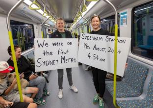 two passengers with placards that reads "We were on the first Sydney Metro, Sydenham Station 19 August 2024  4.54 am 