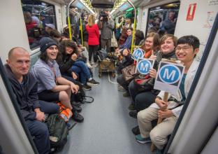 Group of people sitting on the newly opened city line metro. Some holing the metro "M" logo A4 sized placards.