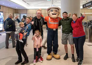 Group of people with two young children cheering with the Metro Mascot