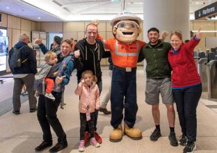 Group of people with two young children cheering with the Metro Mascot