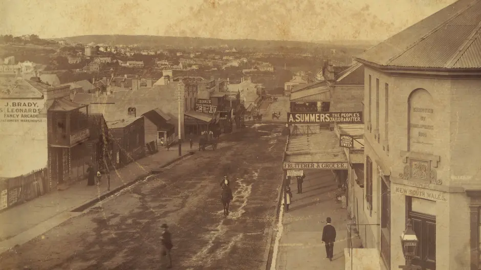 Old and damaged photograph of people walking down a street in North Sydney.