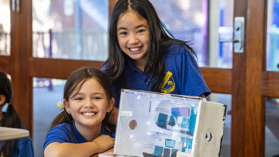 Two girls in school uniforms smiling behind a project they created.