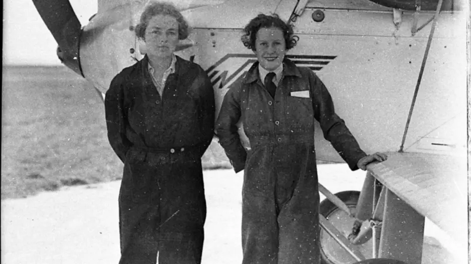 Peggy Kelman (left) with Nancy-Bird Walton (right) standing in front of a plane in pilot gears 