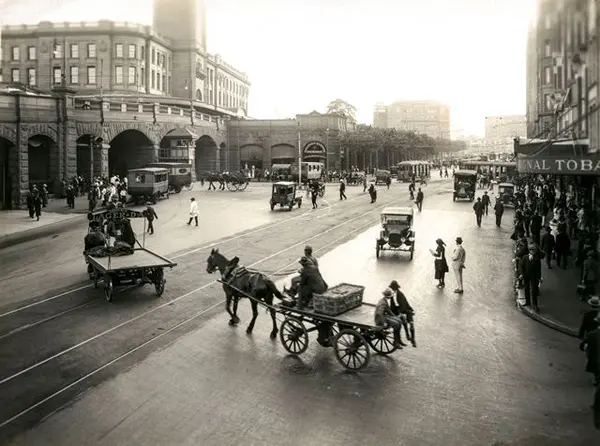 A photo from the City of Sydney Archives: 051080, showing commuters outside of Central station in cars and horse drawn carriages along south of Pitt Street.