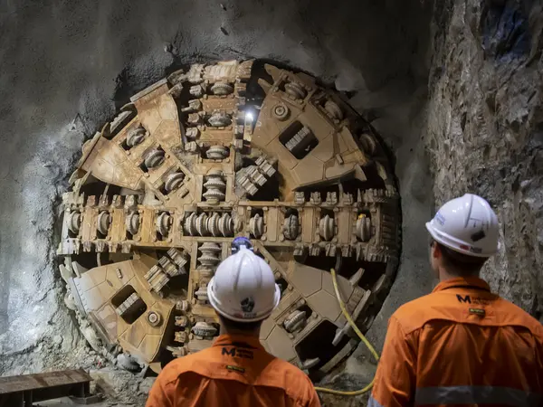 An on the ground view of two Sydney Metro construction workers looking at Tunnel Boring Machine(TBM) Kathleen breakthrough at Blues Point. 