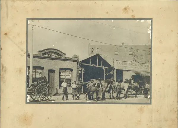 A black and white photo on a faded yellow background of horse and carriages outside of Lambert’s Coach Factory, Crows Nest.