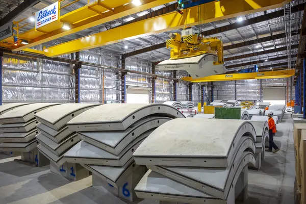 An on the ground shot showing rows on precast concrete segments lined up for production with a machine liftin one of the segments into place at Marrickville precast facility. 