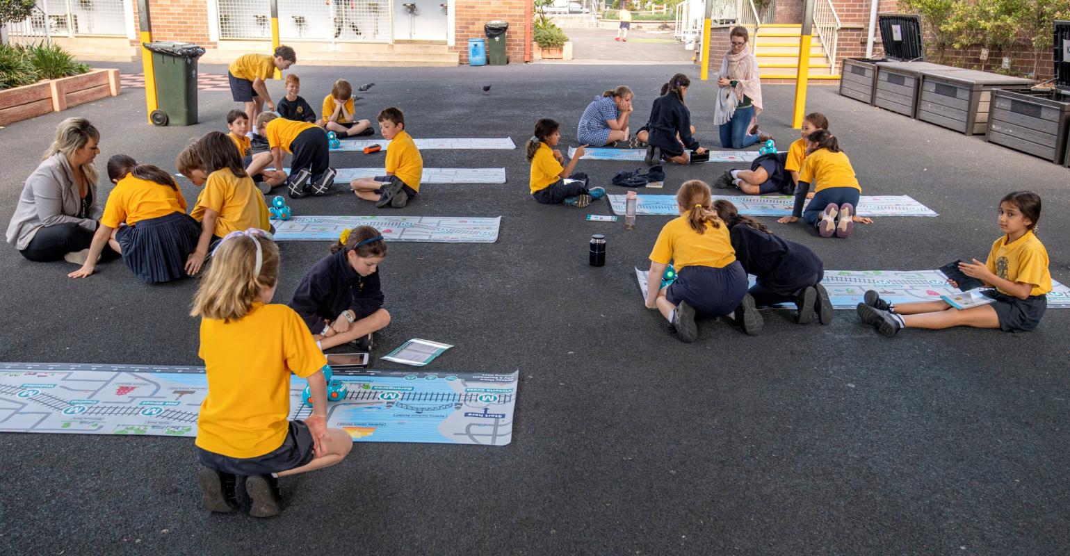 A group of 18 students and their teachers from Petersham Public School using the dash robots that are sitting on top of an alignment map