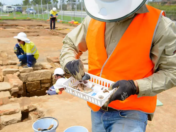 A person in orange high vis vest looks at the artefacts found at the White Hart Inn site.