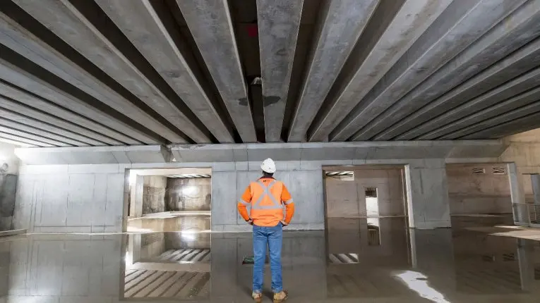 A view from behind showing a man in orange high-vis shirt and hard hat looks on at the Chatswood Dive Cassette Structure with his hands on his hips.