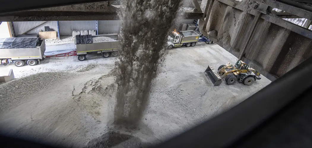 Spoil is falling down into a large mound on the ground while trucks are being filled up to remove it off site.