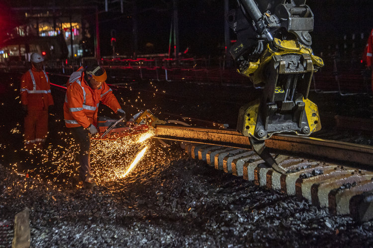 Worker cutting the rail track at night. There is sparks coming off the track and 2 workers in personal protective equipment