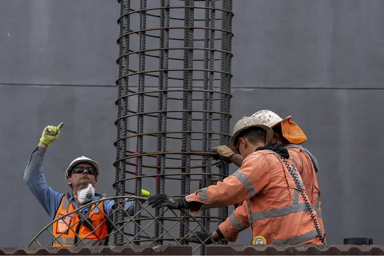 Three construction workers in high viz holding metal piling used to complete piling work at the Northern Connection construction site.