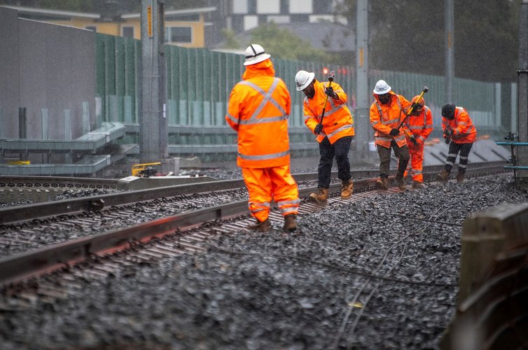 5 construction workers in high viz, using a tool to realign the train track.