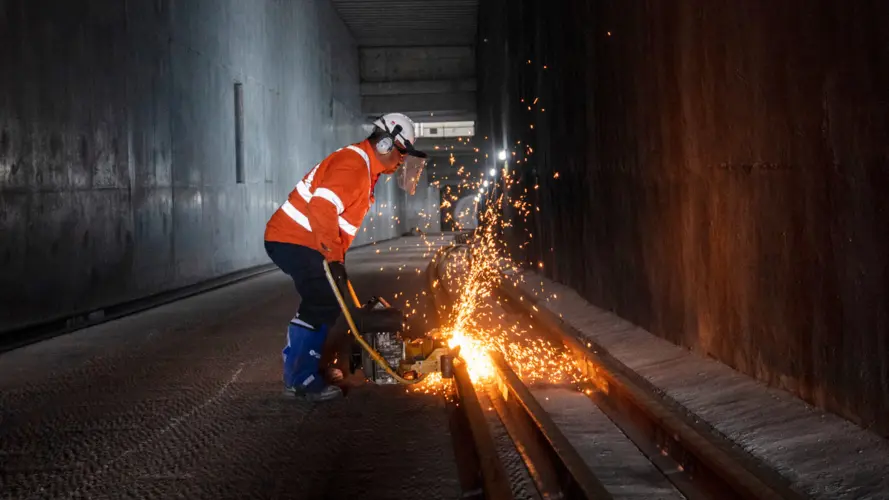 A worker in protective clothing is welding the track at Marrickville Dive site. Sparks can be seen from the welding.