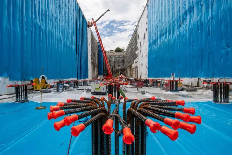 An on the ground view of the Waterloo station box. There are metal pilings and heavy machinery in the background.