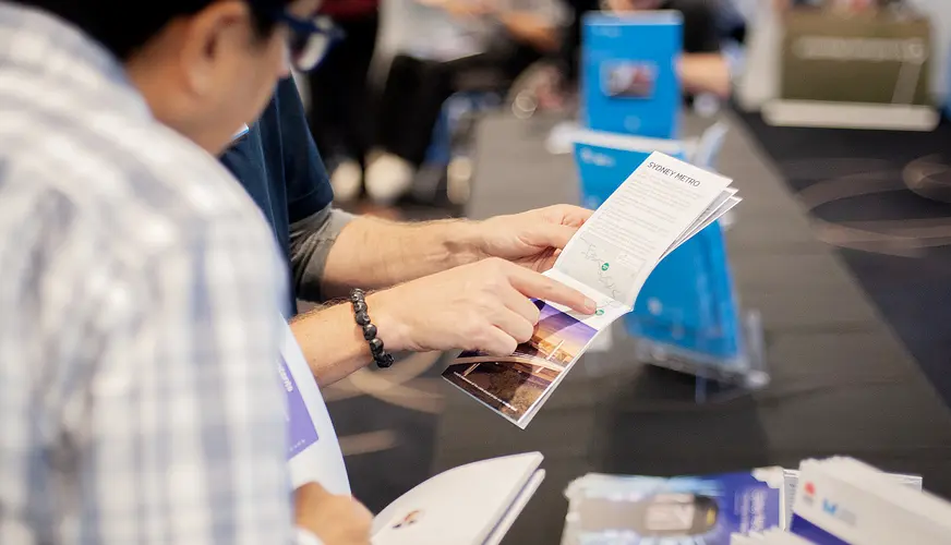 A close up shot showing community members pointing and reading information booklets at a Sydney Metro Community Information Session. 