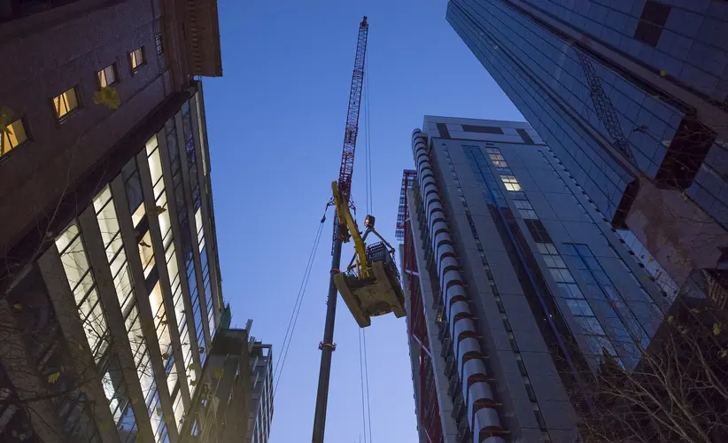 An on the ground view looking up at an excavator is being lifted into place by a crane in between the Sydney sky scrapers in the CBD. 