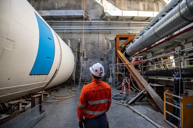 An on the ground view od a construction worker inspecting Tunnel Boring Machine Mabel in place at a Sydney Metro construction site.