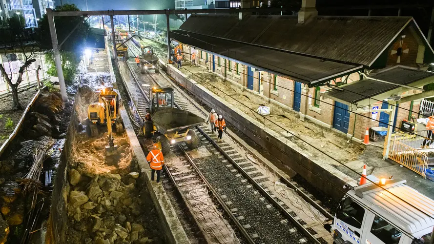 A bird's eye view of construction workers in orange high-vis performing night time track works at Canterbury Station.