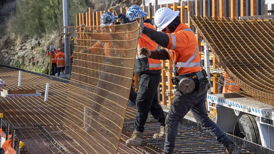 Three construction workers place a sheet of metal rods in place during track works at Dulwich Hill Station.