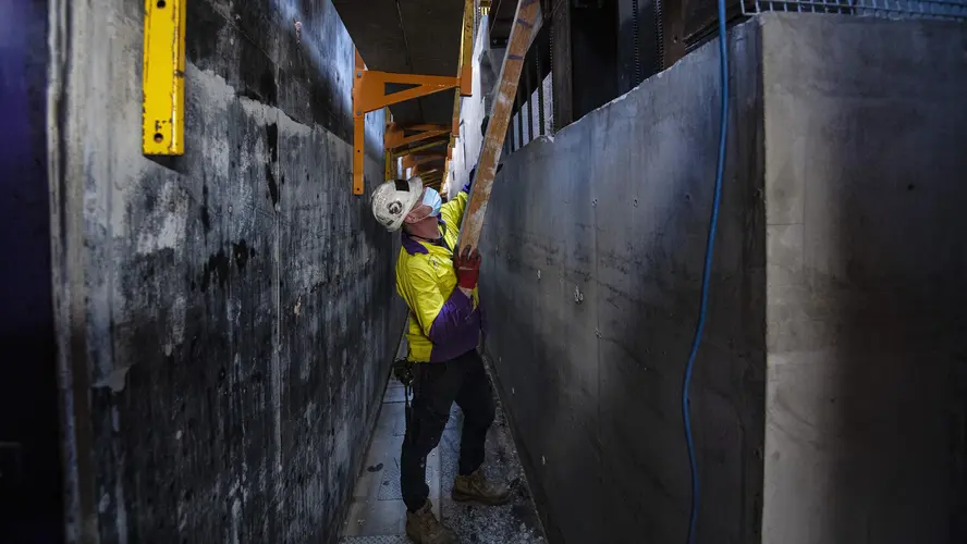 A construction worker is lifting a ladder into place while working on the building cores and internal rooms of Pitt Street Station.