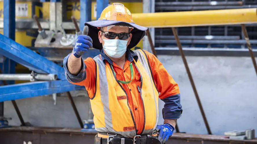 A construction worker in orange high-vis, facemask and sunglasses gives the camera a thumbs-up while on site at Waterloo Station.