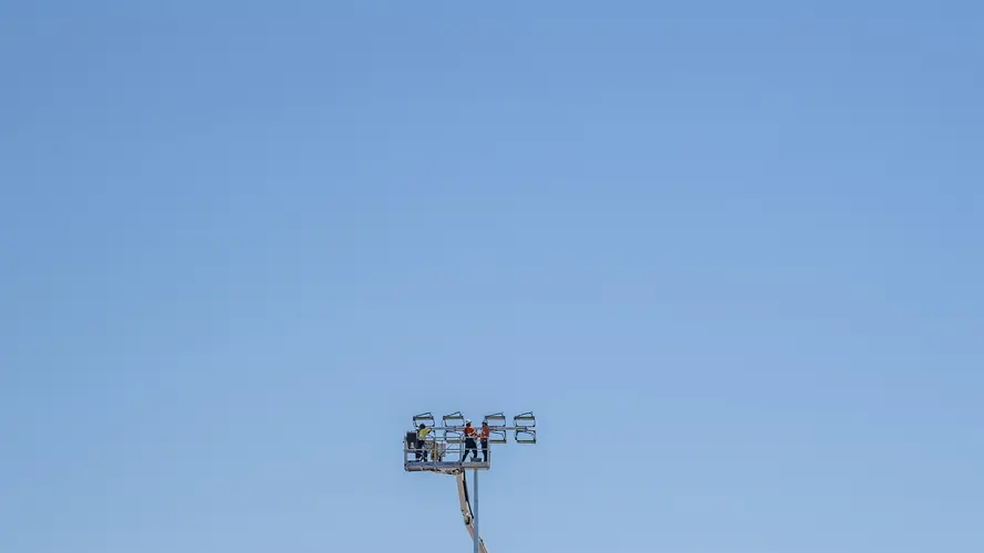 Three construction workers are on top of a tall crane with a clear blue sky in the background.