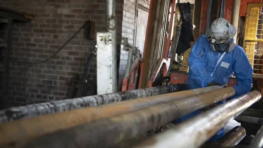 Construction worker wearing a helmet, face mask and PPE suit, pulling a metal pipe.