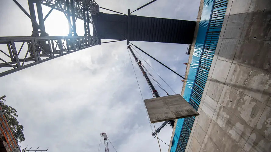 A ground up view of a crane lifting a concrete panel down to B3 level at Sydney Metro's Waterloo Station. 