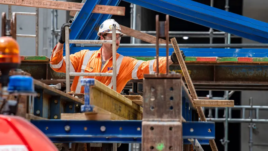 Construction worker on a ladder pulling metal rods on top of a steel metal frame at Sydney Metro's Waterloo Station.