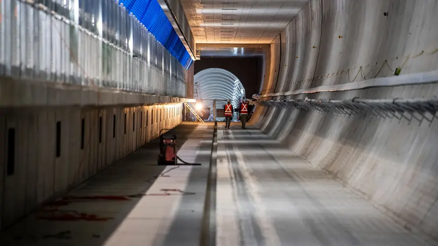 A view of two construction workers walking inside the underground tracks at Victoria Cross Station.