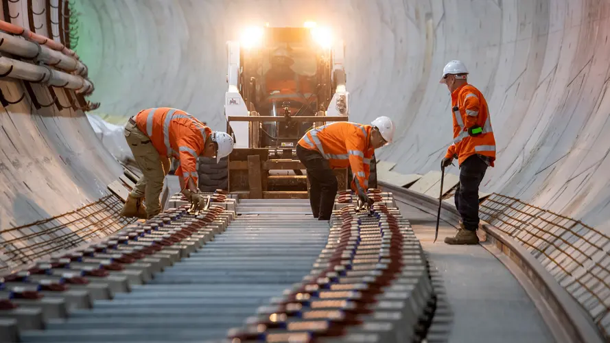 On the ground view of construction workers installing noise attenuating sleepers in the underground tunnel at Sydney Metro's between Martin Place and Barangaroo stations.