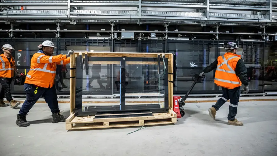 An on the ground view showing construction workers moving the glass panels from the platform screen doors at Sydney Metro's Martin Place Station