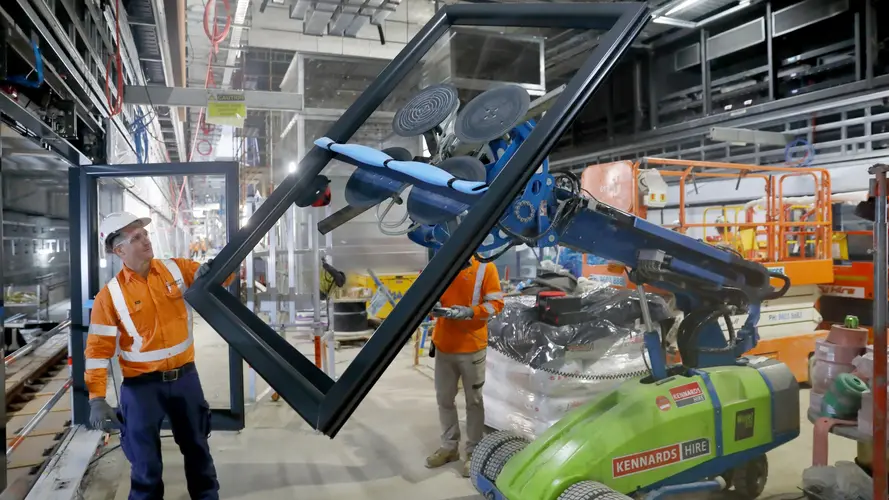 Glass panels from the platform screen doors being moved by a robot and construction workers at Sydney Metro's Crows Nest Station