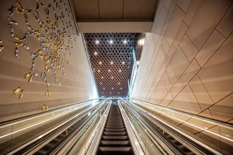  Escalators at Waterloo Station. There's a wall art with golden and silver materials on one side of the escalator wall.