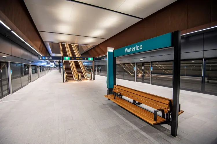 Signage of Waterloo Station in metro brand color, deep bluw just above a seat for passengers. Which is right beside a escalators