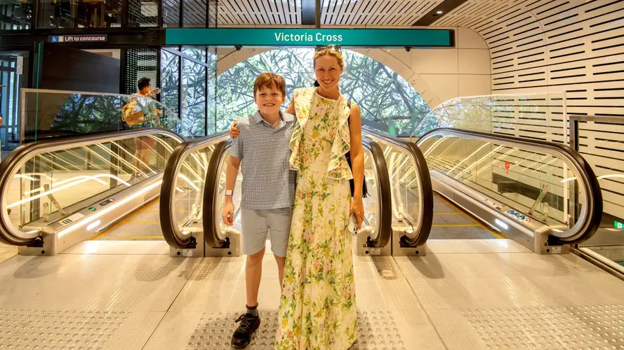 Mother and son standing at the top of the escalators under the station sign