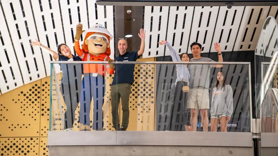 People standing with the mascot with their hands in the air