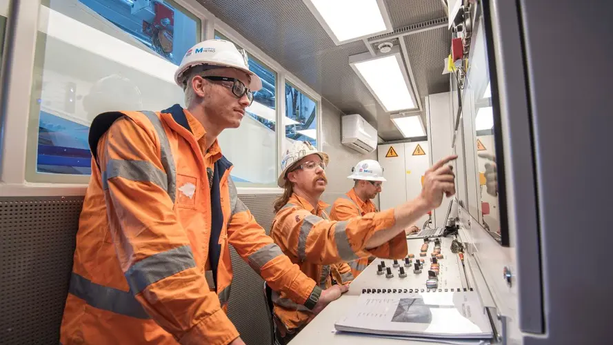 Three Sydney Metro workers in safety gear looking at the screens