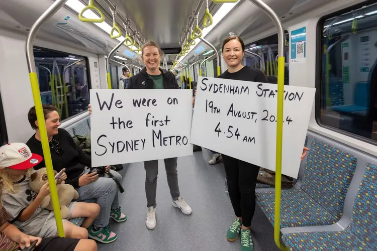 two passengers with placards that reads "We were on the first Sydney Metro, Sydenham Station 19 August 2024  4.54 am 