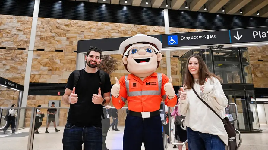 two people taking a photo with the male Metro mascot 