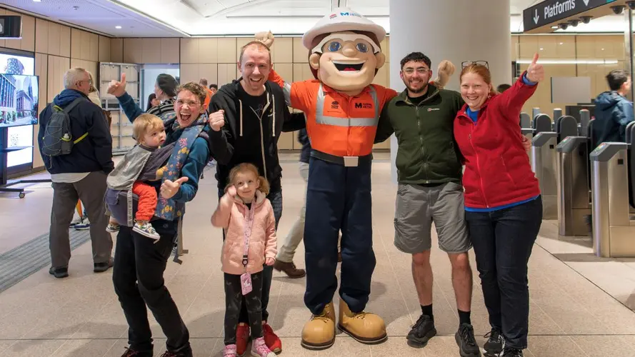 Group of people with two young children cheering with the Metro Mascot